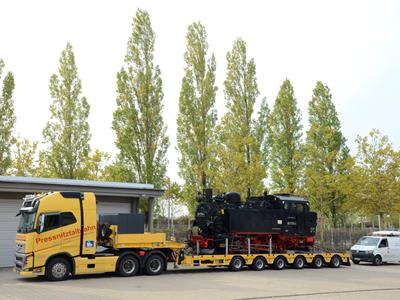 Ancien véhicule ferroviaire à vapeur servant à tirer les wagons d'un train transporté sur une semi-remorque 6 essieux. 